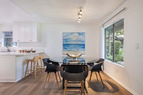 a dining room with a glass table and chairs and a kitchen with a large window